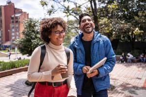 Two people standing outdoors and smiling, holding coffee and a book