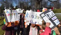 A group of children hold up handmade signs with messages supporting Black Lives Matter and kindness for Black lives during an outdoor demonstration on a sunny day.