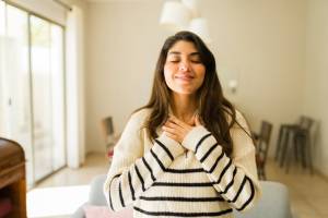 Woman in her living room with her hands over her chest, eyes closed, smiling