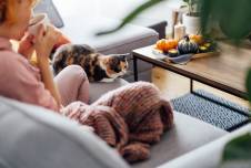 Woman on the couch with cat sipping hot drink with candles nearby