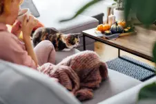 Woman on the couch with cat sipping hot drink with candles nearby