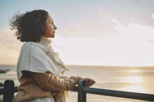 Woman pensively looking out over body of water with sunlight