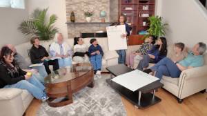 Families sitting on couches with a facilitator holding a poster that says 