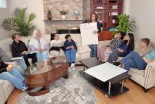 Families sitting on couches with a facilitator holding a poster that says "Bridging Differences is..." 