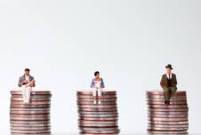 Three tiny figurines, two with babies, sitting on equally tall stacks of coins
