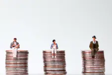 Three tiny figurines, two with babies, sitting on equally tall stacks of coins