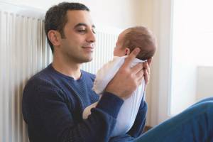 Father sitting on the floor holding and gazing at new baby