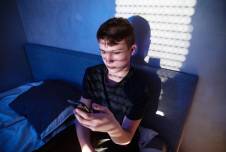 Teen boy sitting on bed looking at smartphone