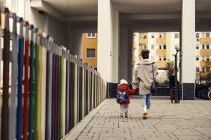Mother walking with toddler to day care, from behind
