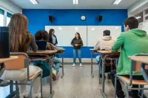 High school student standing at the front of a classroom talking to the class and teacher