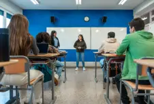 High school student standing at the front of a classroom talking to the class and teacher