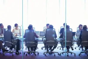 View from behind: about 10 employees sitting at a conference table looking to the right