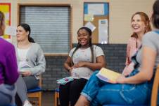 Five women sitting on chairs in a school hallway having a conversation
