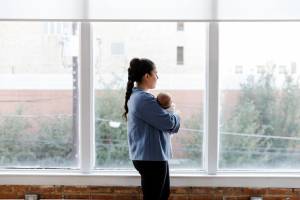 Mom standing holding her baby in front of a set of windows