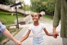 Young girl walking down the street holding hands with two people out of frame