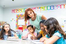 Teacher leaning over desk to help four students with an activity