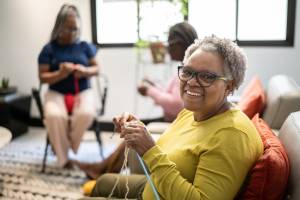 Woman holding knitting and smiling, with two other women in the background