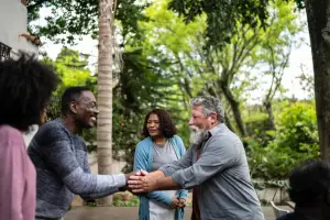 Neighbors shaking hands warmly outdoors while other neighbors look on