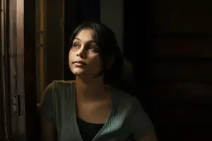 Woman in a dark room looking out a window with light shining on her face