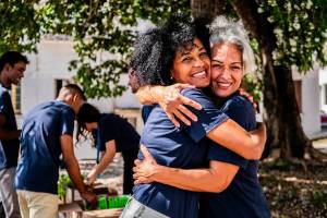 Two volunteers hugging with more people doing volunteer work in the background