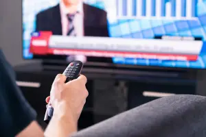Person's hand holding remote watching the news on TV