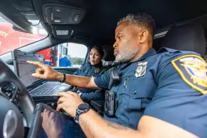 Two police officers looking at screen in the front seat of police car