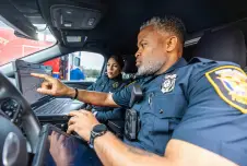 Two police officers looking at screen in the front seat of police car