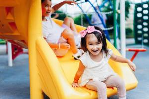 Two girls going down a slide on a jungle gym