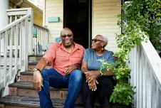 Two older adults sitting on their front steps smiling with sunglasses