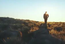Man walking up a grassy hill with sunlight shining in front of him