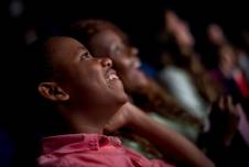 Boy in movie theater looking up at screen and smiling, with other patrons in background