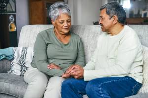 Older couple sitting on the couch, him holding her hand