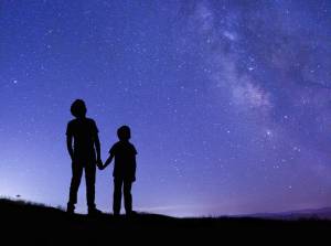 Two kids holding hands looking up at night sky, from behind