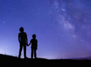 Two kids holding hands looking up at night sky, from behind