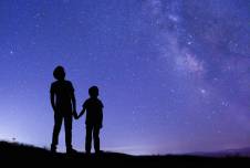 Two kids holding hands looking up at night sky, from behind