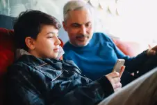 Teen boy and father sitting on couch looking at his smartphone
