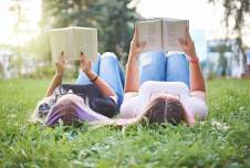 Two women lying on their backs in the grass reading books