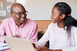 Teacher and student sitting in front of a laptop, making eye contact and smiling