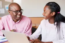 Teacher and student sitting in front of a laptop, making eye contact and smiling