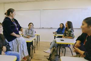 Teacher sitting on desk talking and smiling with group of students