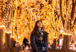 Woman outdoors looking up at vibrant holiday lights on trees