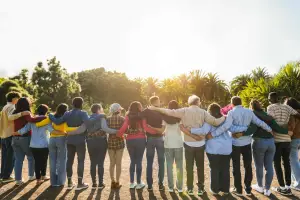 Back view of line of people with their arms around each other in front of setting sun