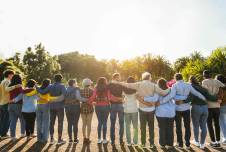 Back view of line of people with their arms around each other in front of setting sun