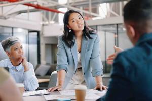Woman standing up at conference table talking to two other colleagues