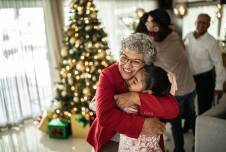 Grandmother hugging granddaughter, with Christmas tree and family in the background