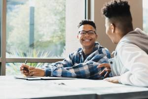 Two students sitting at a desk talking and smiling