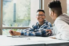 Two students sitting at a desk talking and smiling