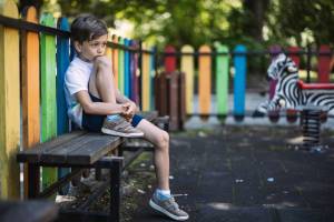 Boy sitting on the playground with one knee up looking sad