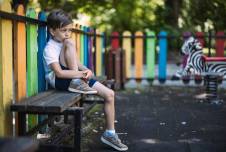 Boy sitting on the playground with one knee up looking sad