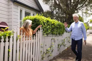 Neighbors waving at each other outdoors over a fence